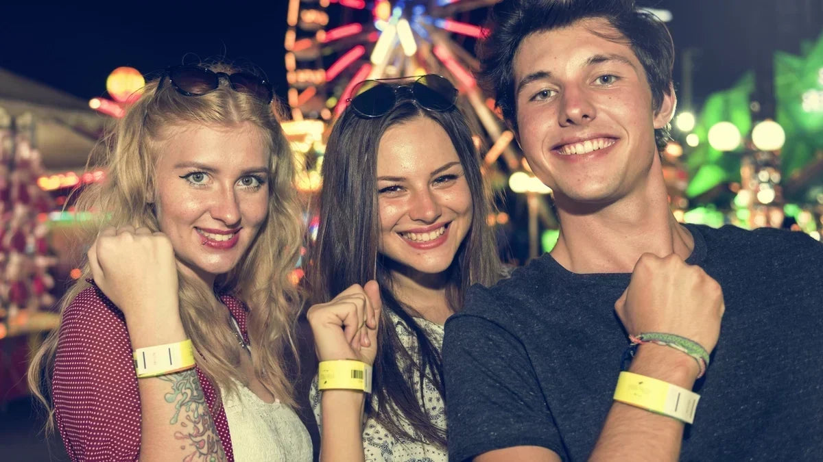 3 people smiling and showing their wristbands in front of a fair. 