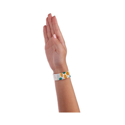 wrist wearing a white tyvek wristband with silver, gold and green leaves pattern