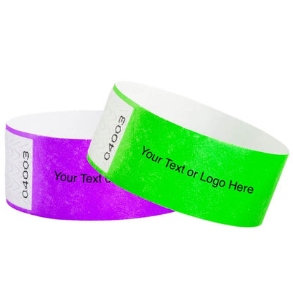 Two customizable qwik fit tyvek 1" wristbands, one purple and one neon green.